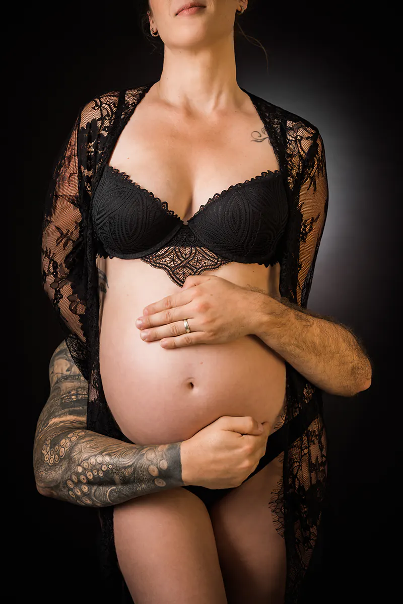 Séance photo grossesse à Ollioules : portrait de couple intime en studio, future maman en lingerie noire et dentelle enlacée par le futur papa.