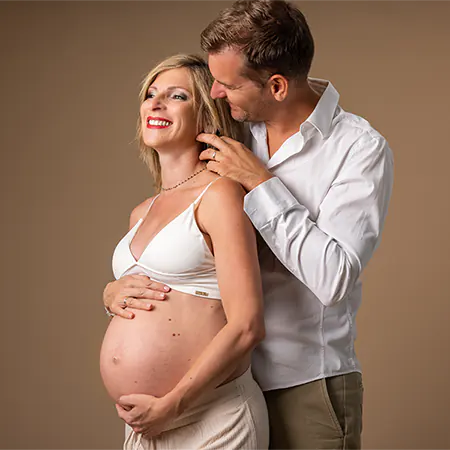 Séance photo grossesse Ollioules : portrait élégant en studio d'une femme enceinte assise, portant une longue robe verte fluide et tenant son ventre.