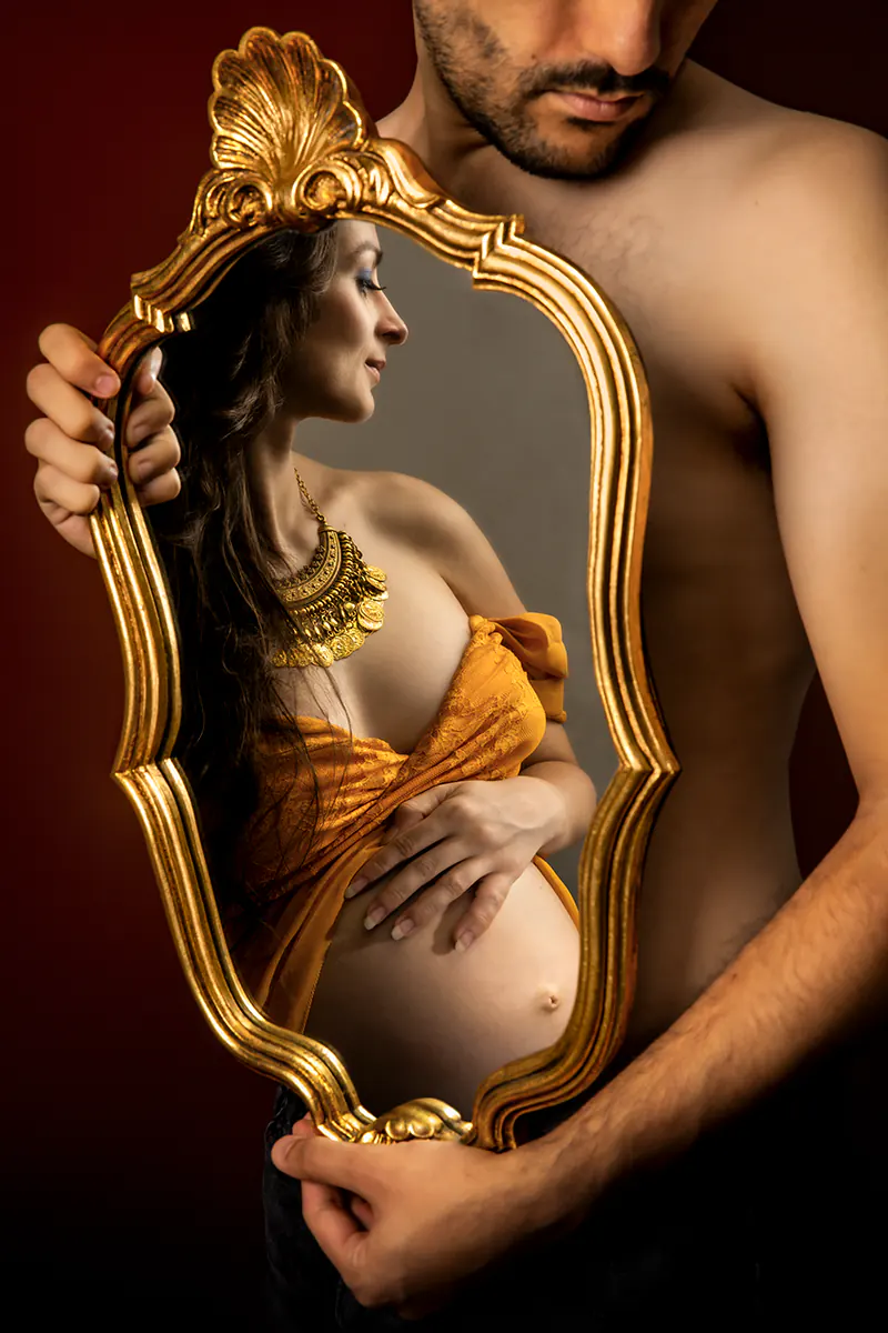 Séance photo grossesse à Ollioules : portrait de couple original en studio avec le reflet de la future maman dans un miroir doré vintage.