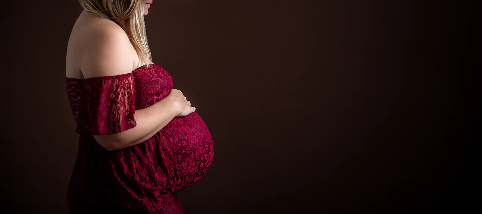 Séance photo grossesse à Ollioules : future maman en robe de dentelle bordeaux posant en studio.